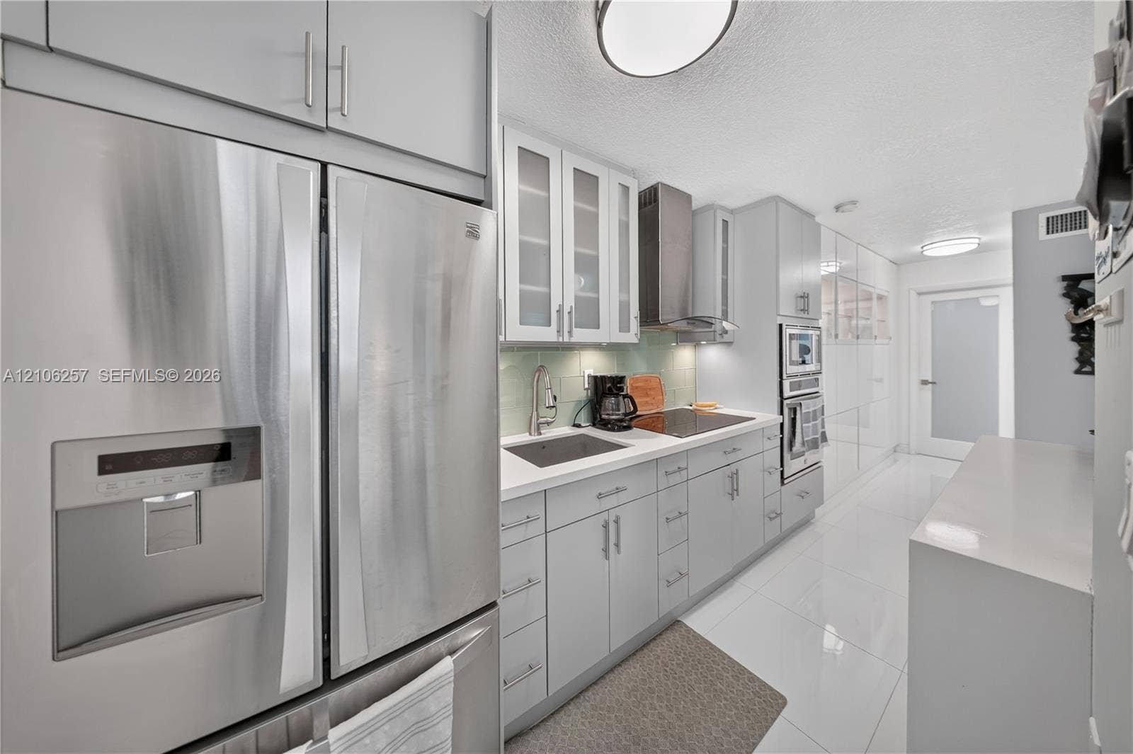 Kitchen featuring stainless steel appliances, glass-front cabinetry, integrated wall oven, solid surface countertops, and glossy tile flooring