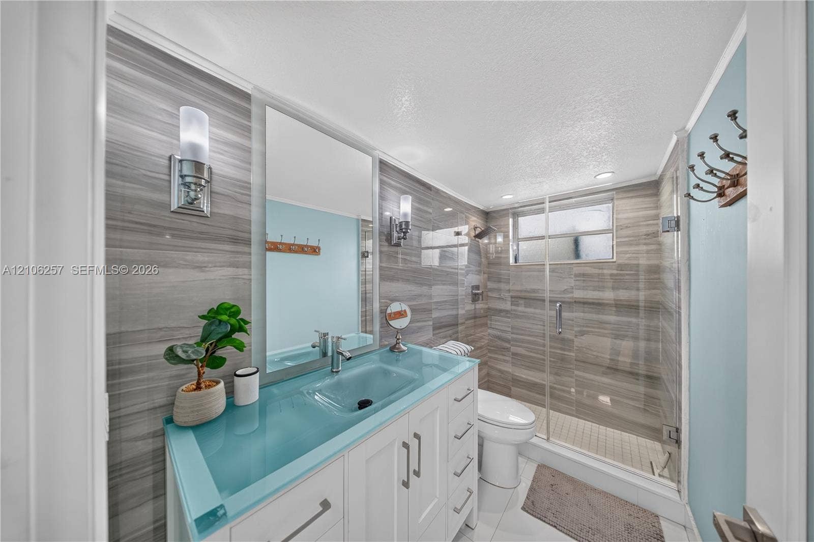 Bathroom featuring floor-to-ceiling wood-finish wall tile, a glass-topped vanity with an integrated sink, two wall-mounted metallic light fixtures, and a walk-in shower with a glass enclosure