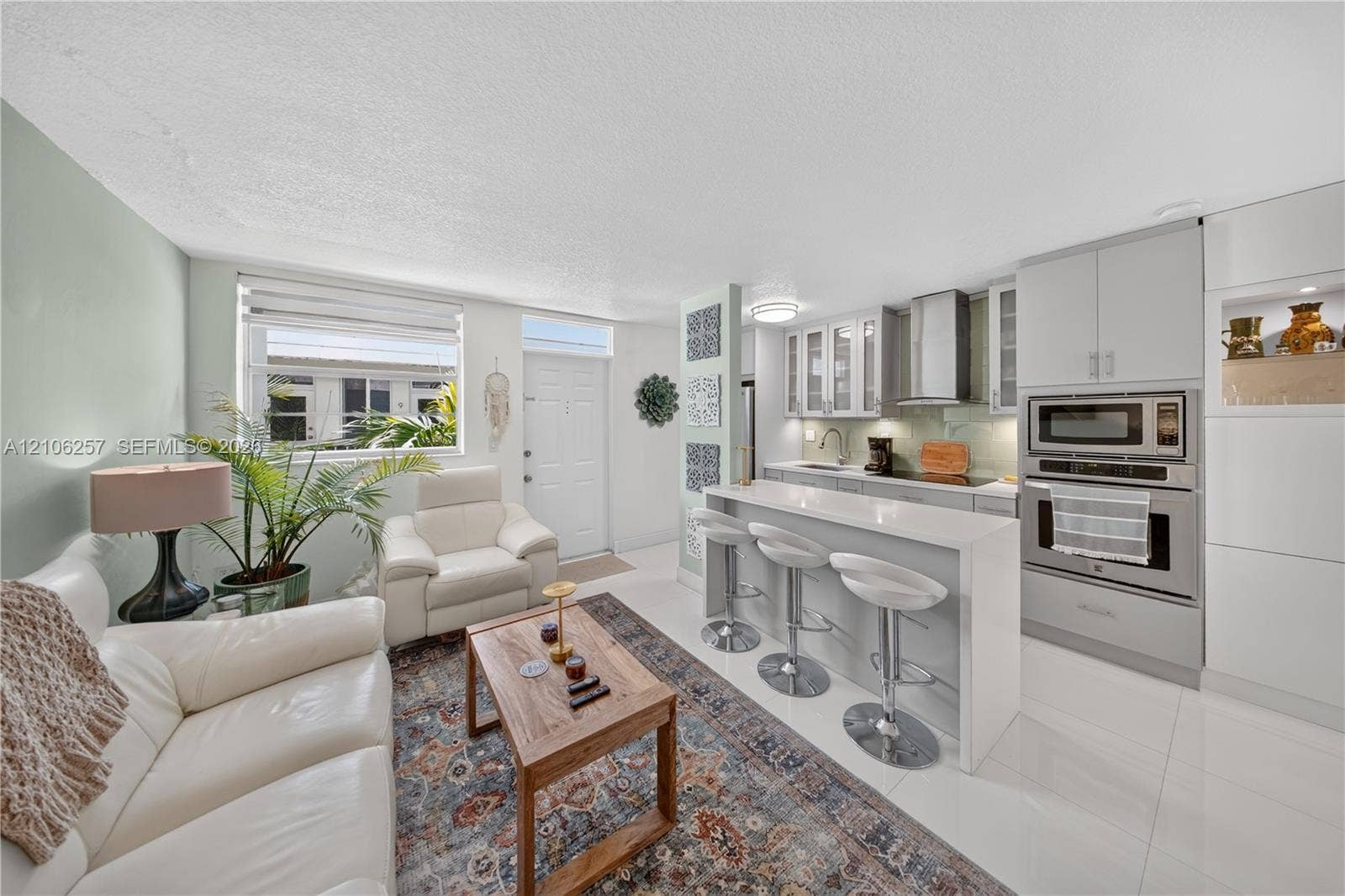 Kitchen featuring light gray cabinetry, a breakfast bar with stone-style countertop, stainless steel built-in wall oven and microwave, stainless steel range hood, and tile flooring