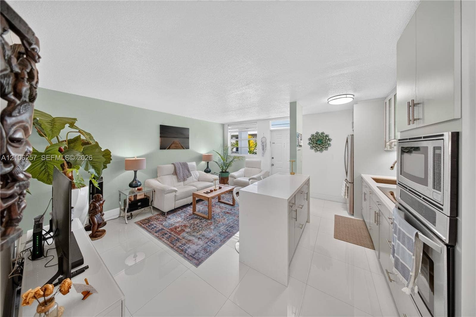 Open-concept living space featuring high-gloss tile flooring, white shaker cabinetry, a central island with a solid-surface countertop, and integrated stainless steel wall oven and microwave