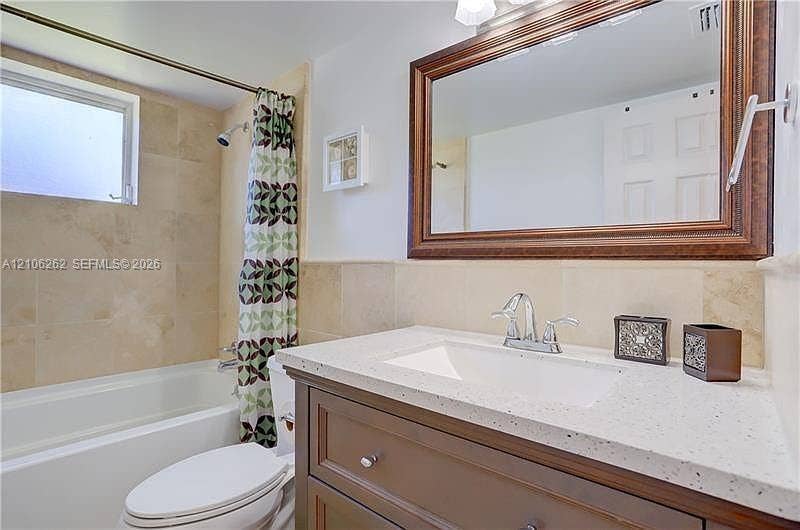 2212 NE 1st Way, #101, Boynton Beach, FL 33435 Bathroom featuring a vanity with speckled countertop, integrated sink, and polished metal faucet, complemented by a wall-mounted framed mirror and a tile-surround tub with a shower head