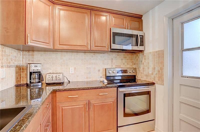2212 NE 1st Way, #101, Boynton Beach, FL 33435 Kitchen featuring natural wood cabinetry, stone-finish countertops, stainless steel appliances, and a tiled backsplash