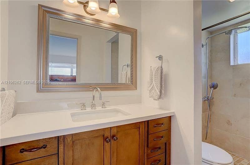 2212 NE 1st Way, #101, Boynton Beach, FL 33435 Bathroom vanity with wood-finish cabinetry, solid surface countertop, rectangular undermount sink, three-light wall-mounted fixture, and tile-surround shower