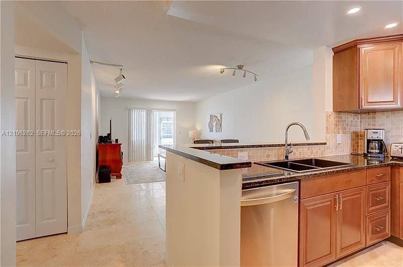 2212 NE 1st Way, #101, Boynton Beach, FL 33435 Kitchen featuring wood-finish cabinetry, stone-surface countertops, mosaic tile backsplash, stainless steel dishwasher, and tile flooring