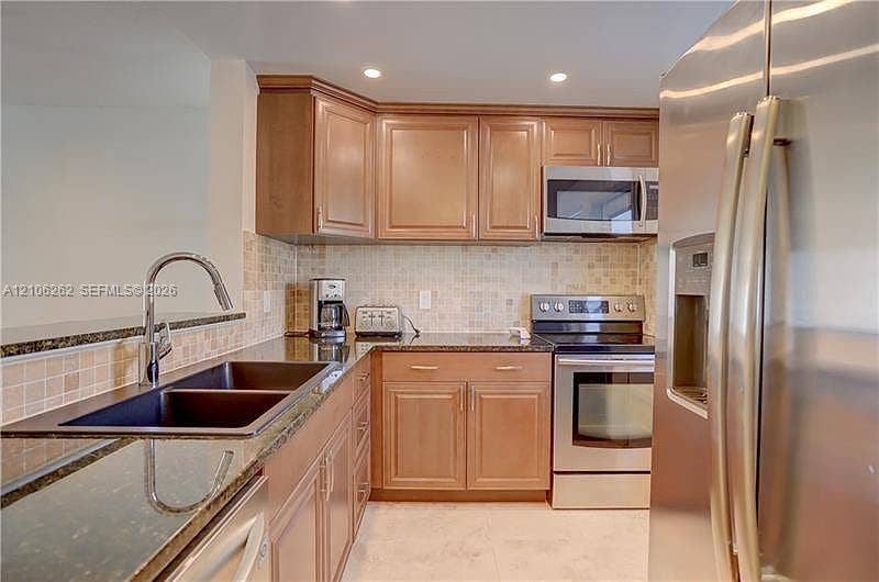 2212 NE 1st Way, #101, Boynton Beach, FL 33435 Kitchen featuring wood cabinetry, stone countertops, square-tile backsplash, stainless steel appliances, and a dual-basin undermount sink with a high-arch faucet