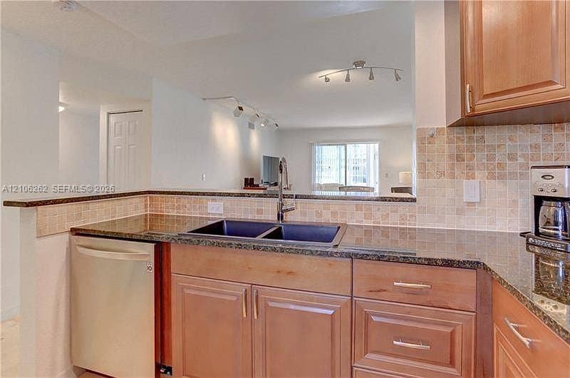 2212 NE 1st Way, #101, Boynton Beach, FL 33435 Kitchen featuring custom wood cabinetry, dark stone countertops, a mosaic tile backsplash, a stainless steel dishwasher, and a dual-basin sink with a gooseneck faucet