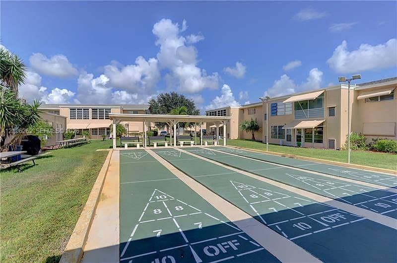 2212 NE 1st Way, #101, Boynton Beach, FL 33435 Outdoor shuffleboard courts featuring a covered pavilion, multi-unit building exterior with beige stucco, and manicured green space