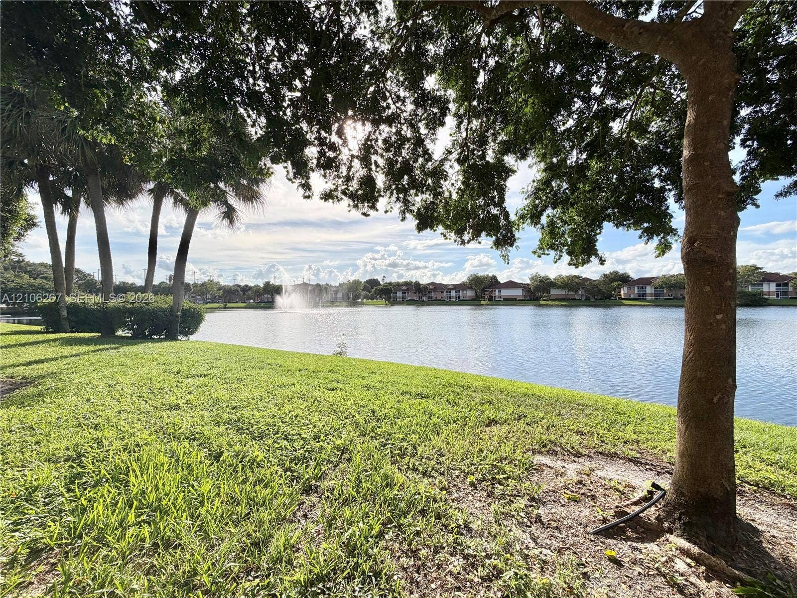 Waterfront parcel featuring a manicured lawn, mature shade trees, established landscaping, and a central water fountain