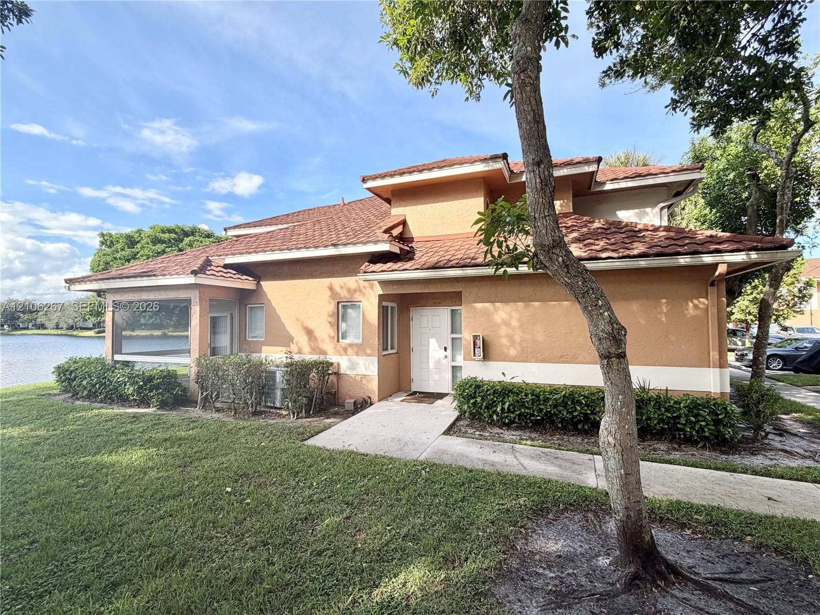Two-story stucco exterior featuring a tiered tile roof, screened-in enclosure, and waterfront positioning