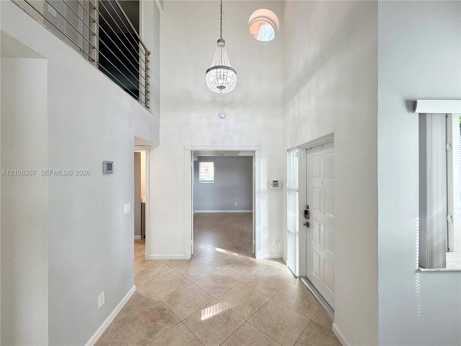 Double-height ceiling entryway featuring tiled flooring, a decorative chandelier, an architectural circular window, and a metal horizontal-bar railing