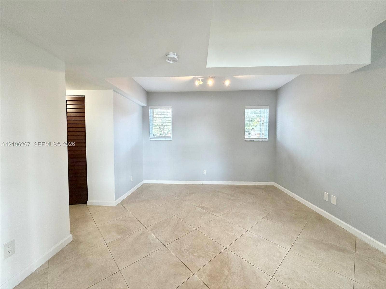 Neutral-toned ceramic tile flooring, dual windows with blinds, recessed track lighting, and a dark wood-finish louvered closet door