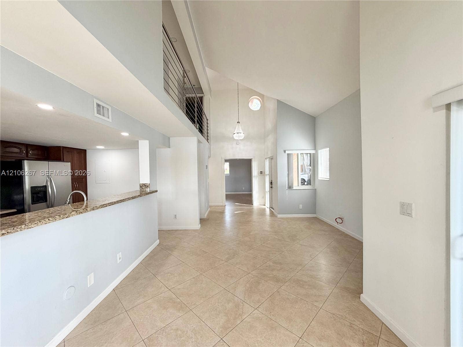 High-ceiling living area featuring tile flooring, a mezzanine level with metal railings, a kitchen peninsula with a stone-finish countertop, and pendant lighting