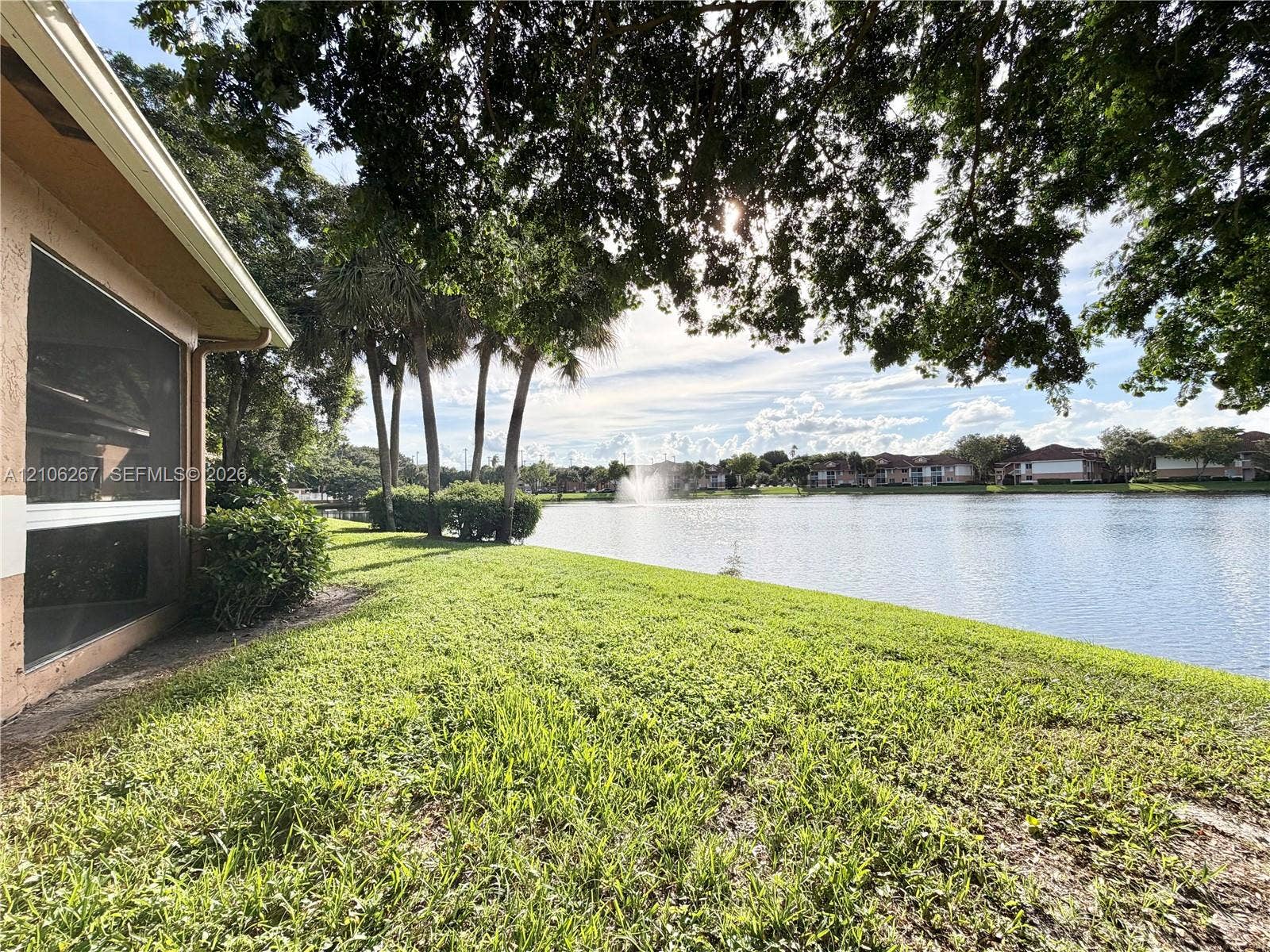 Waterfront grounds featuring mature palms, manicured lawn, established shrubbery, and a central water feature