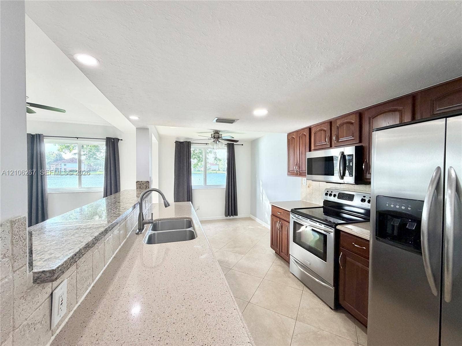Kitchen featuring a stone-composite breakfast bar with an undermount dual-basin sink, wood-finish cabinetry, stainless steel appliances, and tile flooring