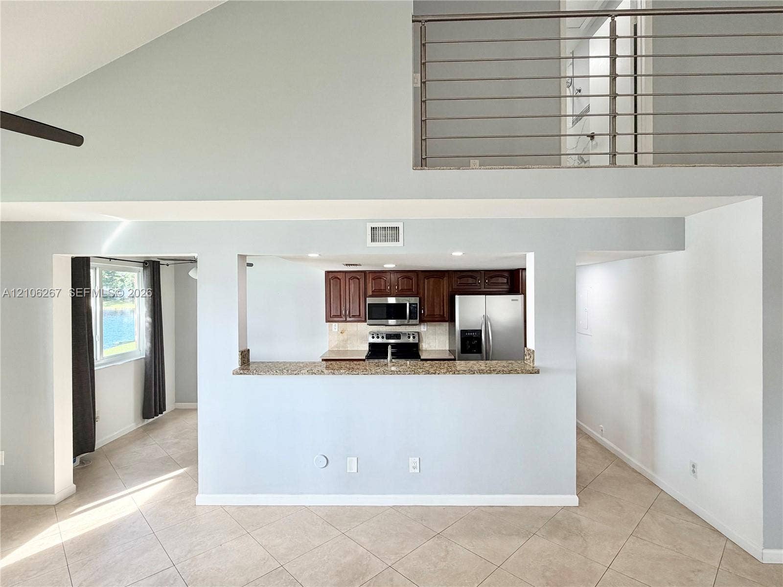Vaulted ceilings, metal horizontal railing, tile flooring, pass-through breakfast bar with stone-finish countertop, and stainless steel kitchen appliances