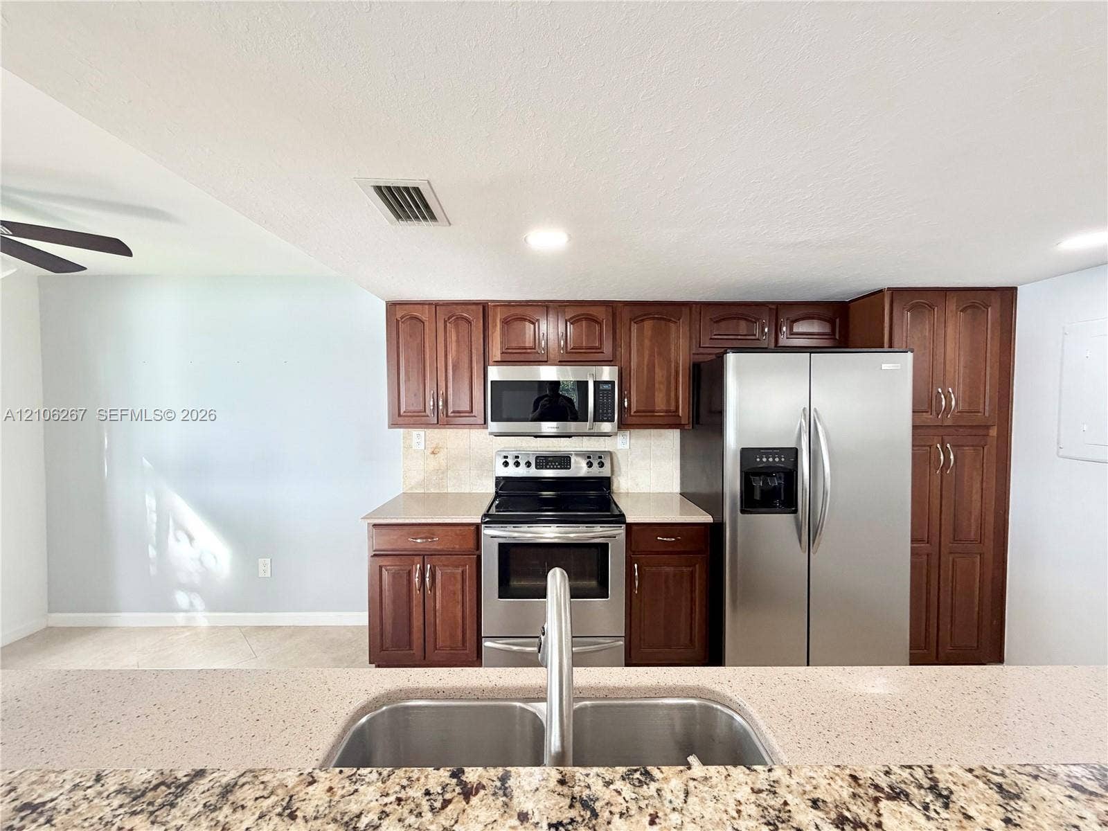 Kitchen featuring wood cabinetry, stainless steel appliances, a double-basin undermount sink, and a stone-surface breakfast bar