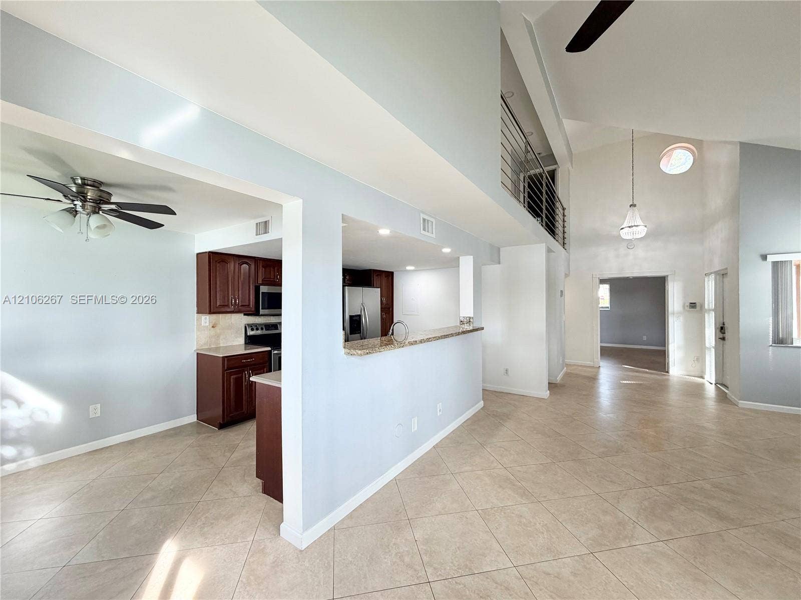 Vaulted ceilings, tiled flooring, open-concept kitchen with stone countertops, dark wood cabinetry, and a metal-railed mezzanine