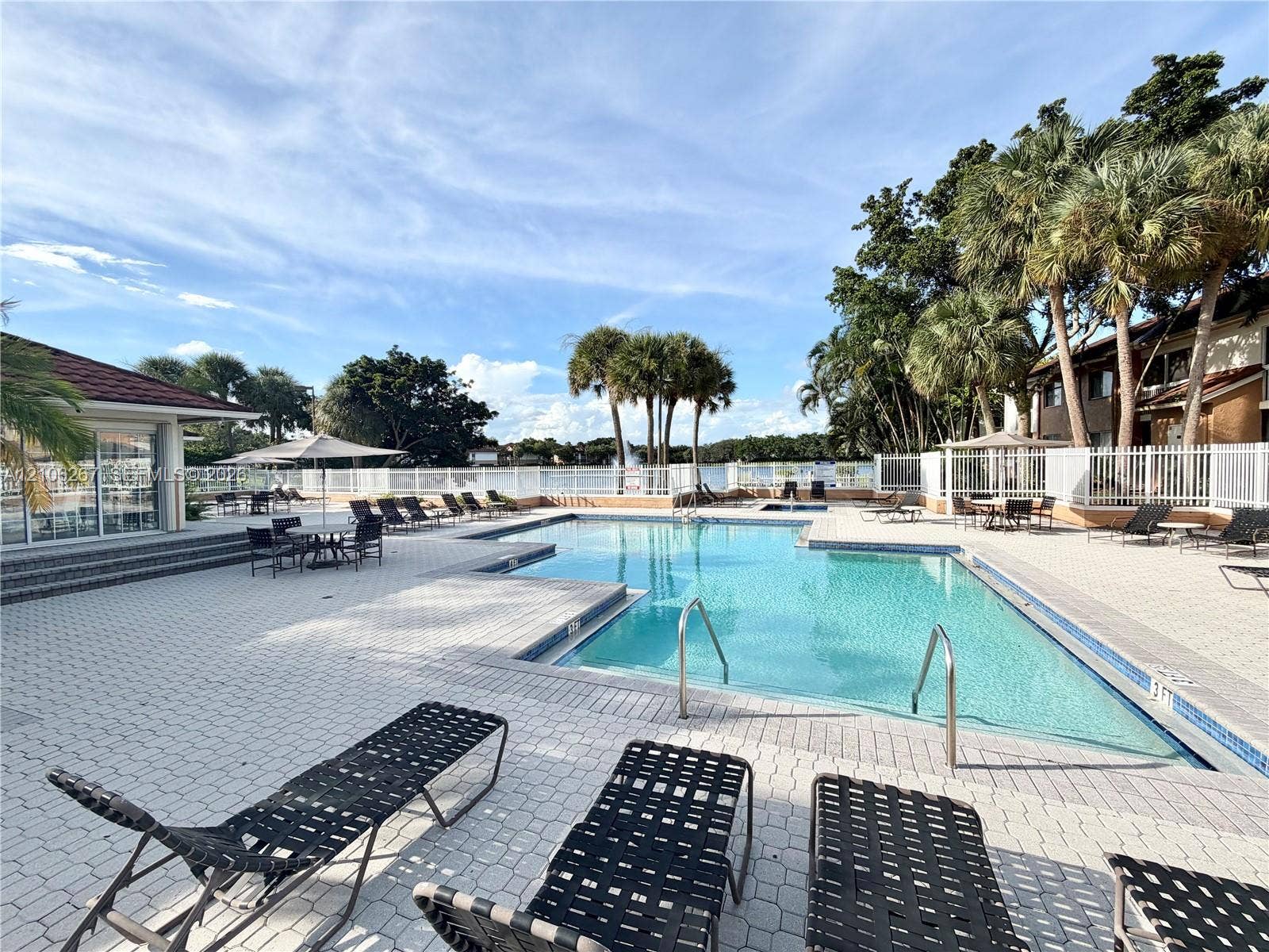 Swimming pool with tiled decking, metal handrails, and surrounding perimeter fencing