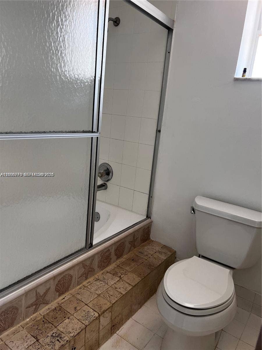 2410 NE 10th Street, #123, Hallandale Beach, Hallandale Beach, FL 33009 Bathtub and shower combination featuring a metal-framed glass enclosure, white wall tiling, and a decorative tile surround with a coastal motif