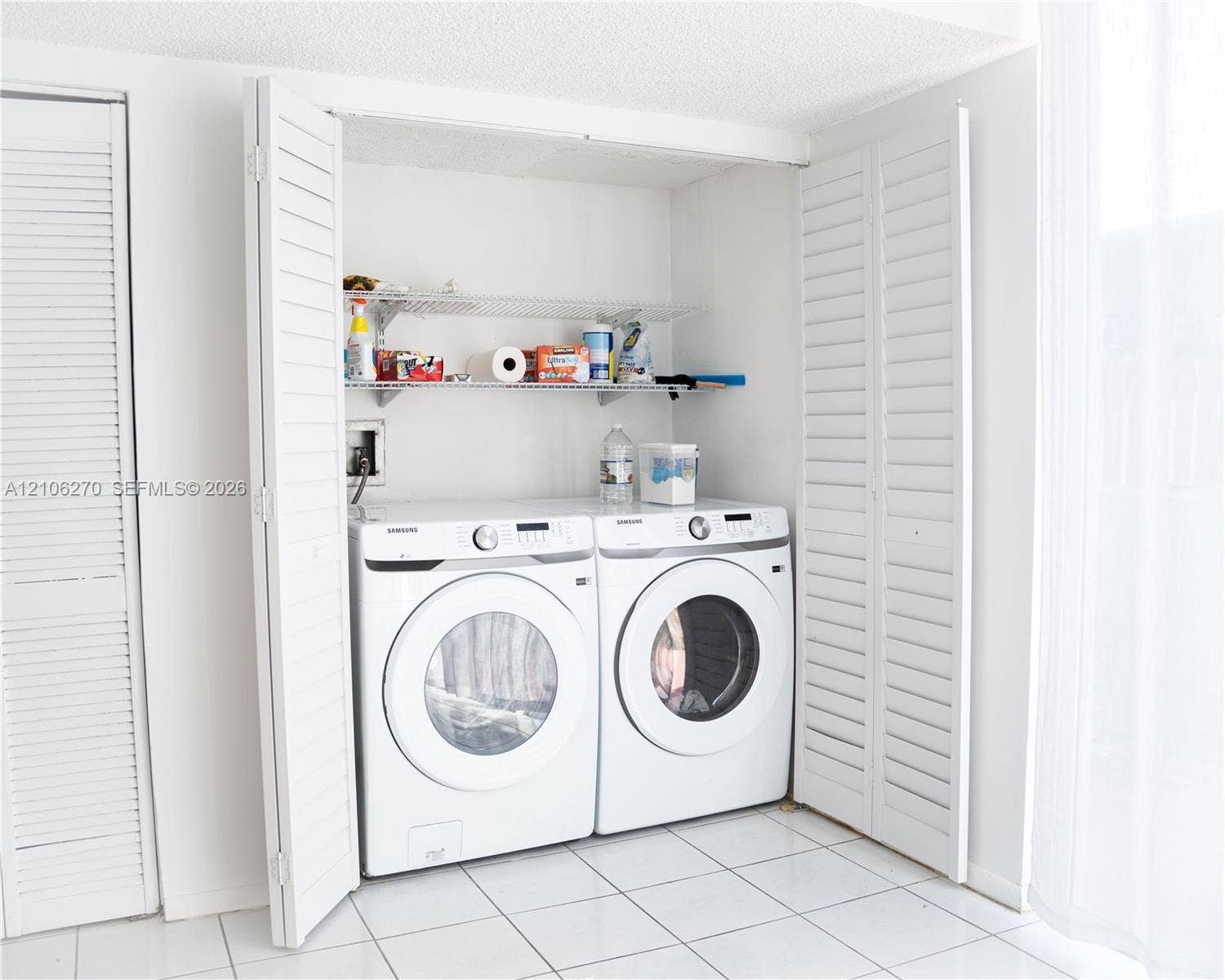 2410 NE 10th Street, #123, Hallandale Beach, Hallandale Beach, FL 33009 Laundry alcove featuring white louvered bifold doors, tile flooring, and integrated metal wire shelving