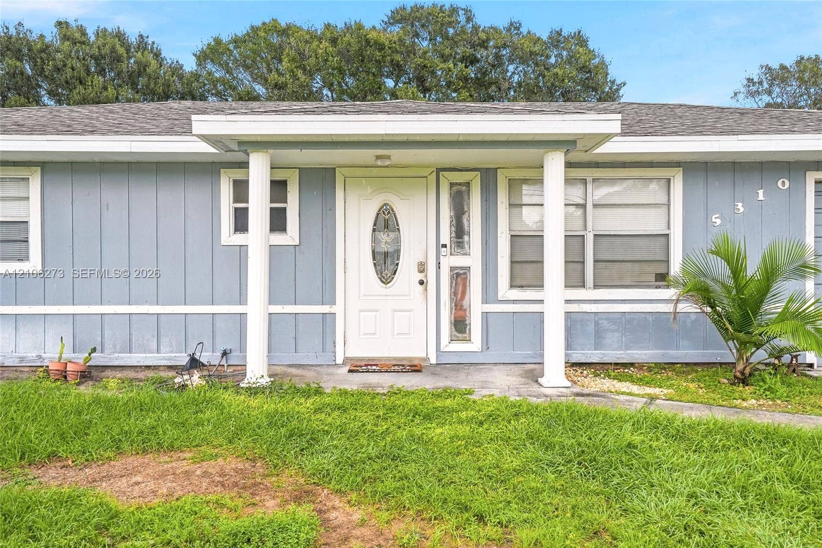 5310 Seagrape Drive, Fort Pierce, FL 34982 Single-story exterior featuring vertical siding, a covered entryway with structural columns, and a front door with decorative oval glass inlay and sidelight