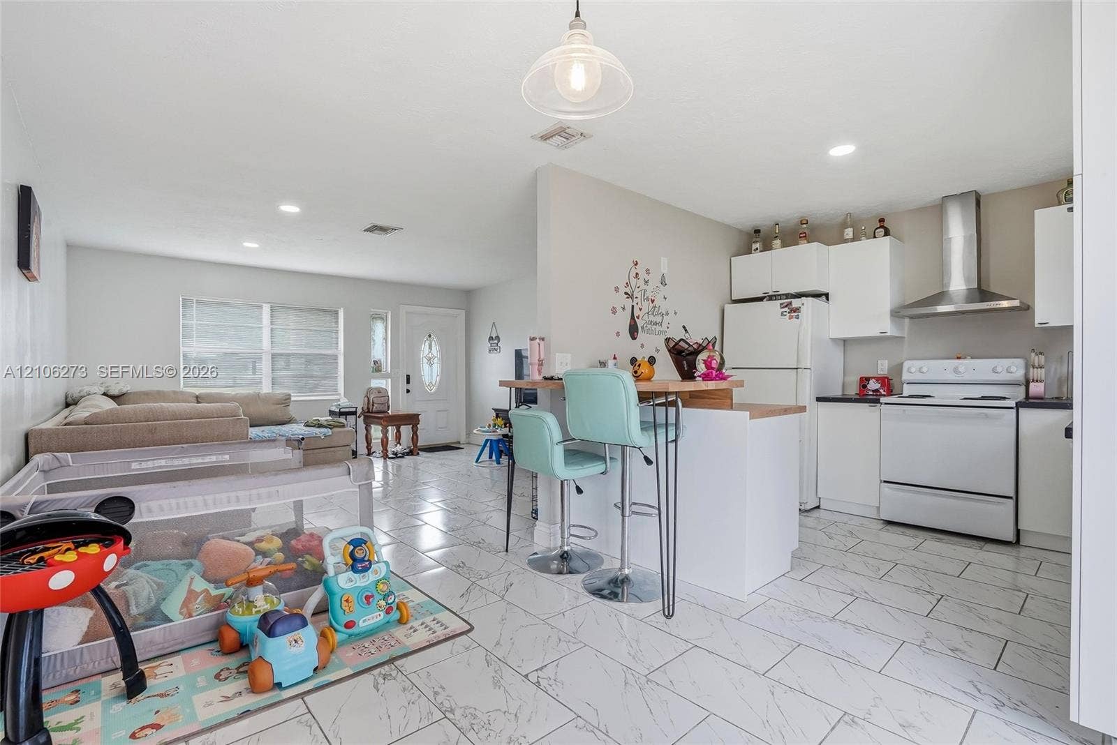 5310 Seagrape Drive, Fort Pierce, FL 34982 Open-concept interior featuring large-format tile flooring, white cabinetry, a stainless steel range hood, and a built-in breakfast bar