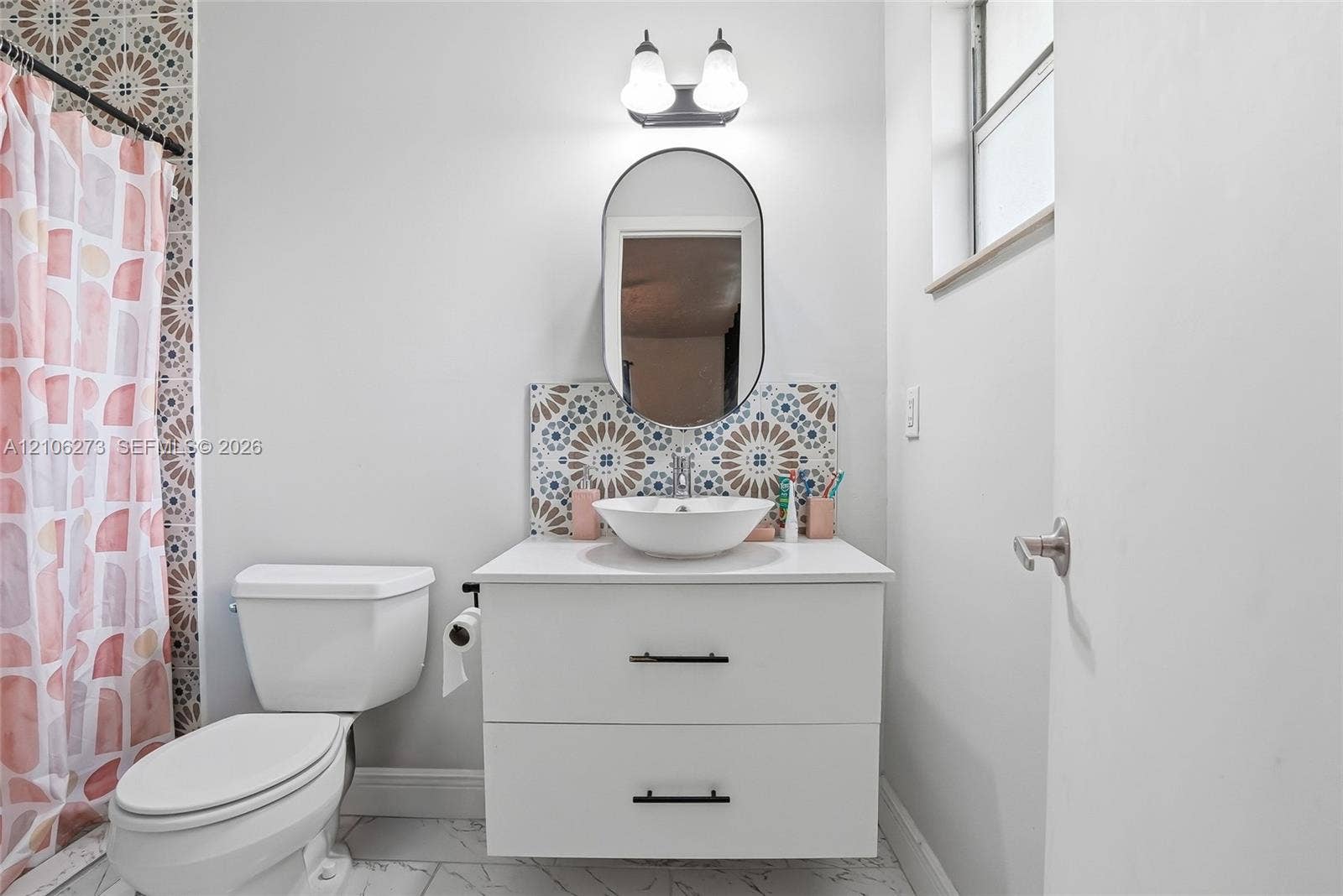 5310 Seagrape Drive, Fort Pierce, FL 34982 White vanity with a round vessel sink, matte black hardware, oval wall-mounted mirror, decorative geometric tile backsplash, and tile flooring