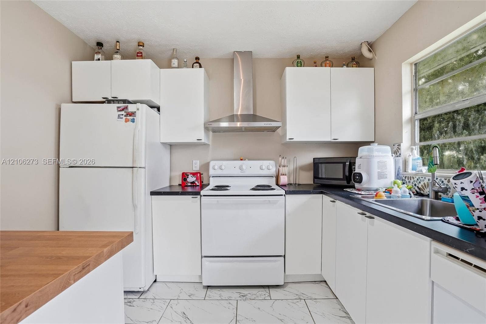5310 Seagrape Drive, Fort Pierce, FL 34982 Kitchen featuring white cabinetry, dark countertops, stainless steel chimney-style range hood, stainless steel sink with gooseneck faucet, and stone-finish tile flooring