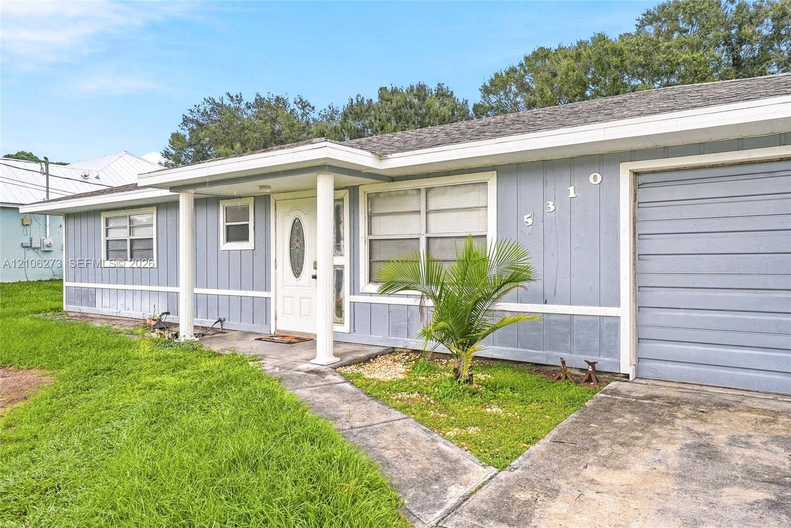 5310 Seagrape Drive, Fort Pierce, FL 34982 Single-story exterior featuring light-toned vertical siding, a covered entryway with structural columns, a paneled front door with an oval glass insert, and an attached garage