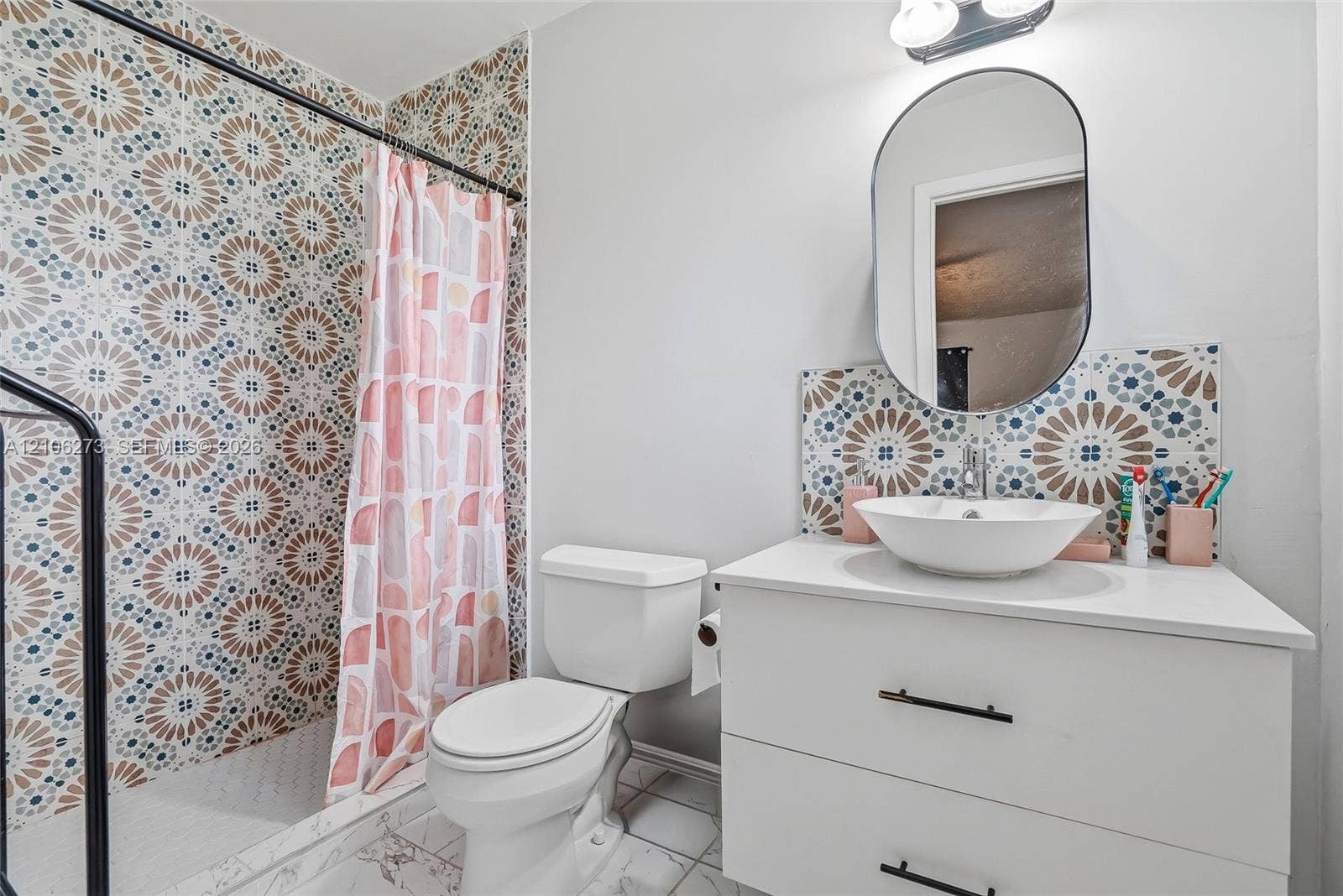 5310 Seagrape Drive, Fort Pierce, FL 34982 Bathroom featuring patterned tile wall surrounds, a white vanity with two storage drawers, a round vessel sink, an oval mirror, and an overhead light fixture