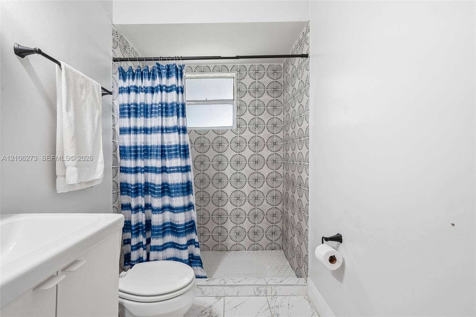 5310 Seagrape Drive, Fort Pierce, FL 34982 Shower alcove featuring patterned wall tile, white floor tile with gray veining, a built-in horizontal window, a wall-mounted matte black towel bar, and a matte black toilet paper holder