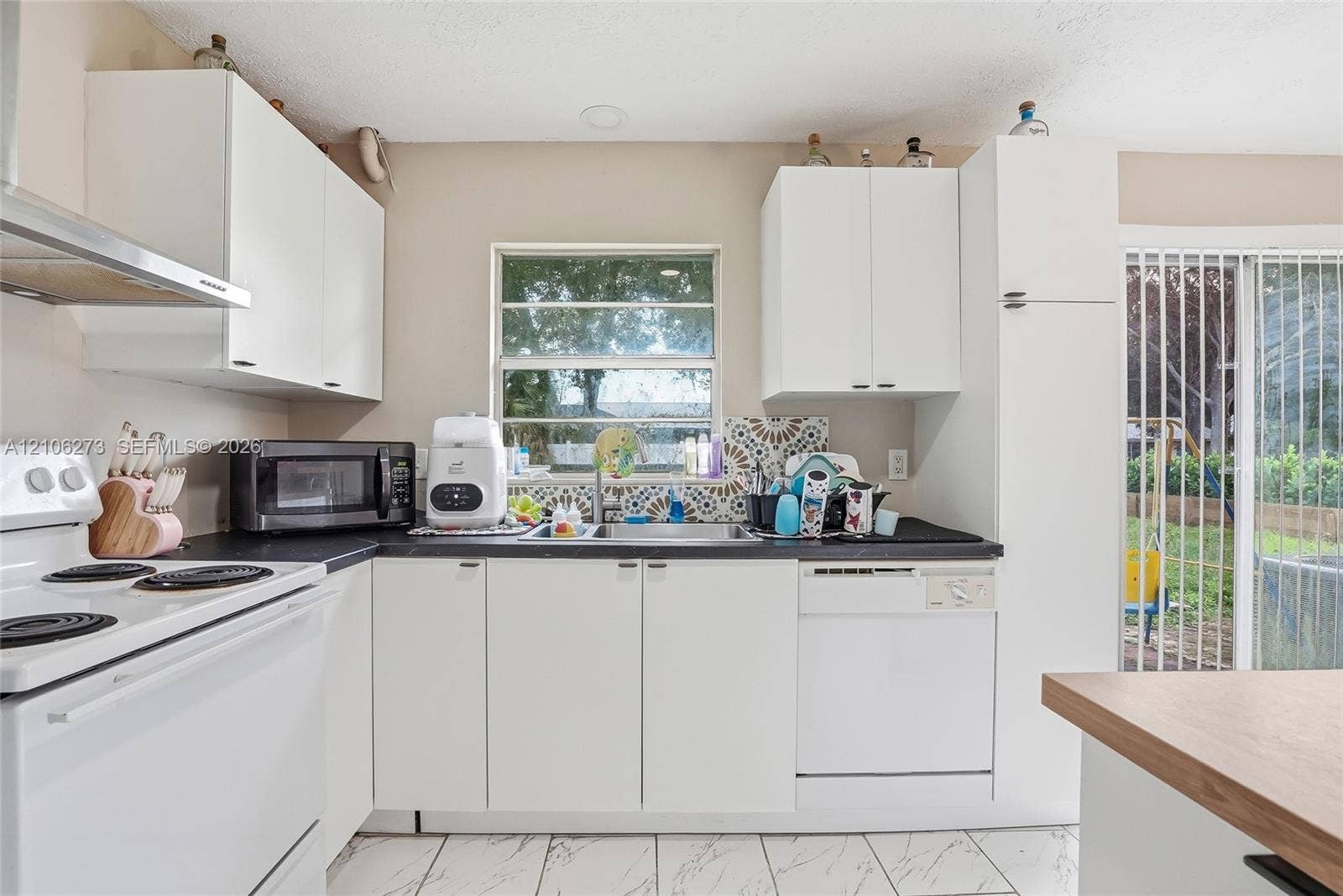 5310 Seagrape Drive, Fort Pierce, FL 34982 Kitchen featuring white shaker-style cabinetry, matte black countertops, stainless steel sink with a decorative tiled backsplash, white appliance suite, and light-toned tile flooring