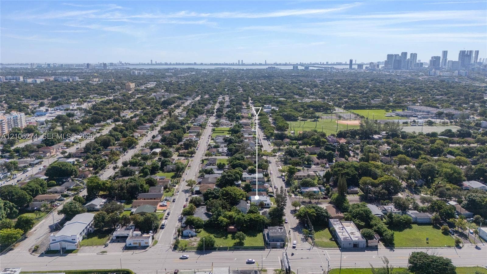 1601 NW 50th Street, Miami, FL 33142 Aerial perspective highlighting the property location within a tree-lined residential area, featuring proximity to urban skyline scenery and nearby recreational green space
