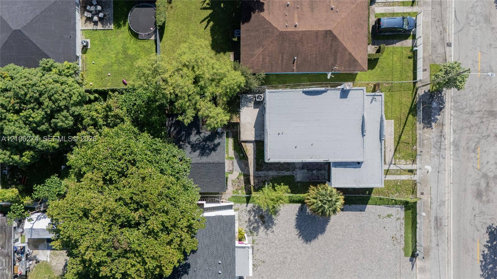 1601 NW 50th Street, Miami, FL 33142 Aerial perspective featuring a flat-roof residence, extensive gravel parking area, mature canopy trees, and fenced perimeter