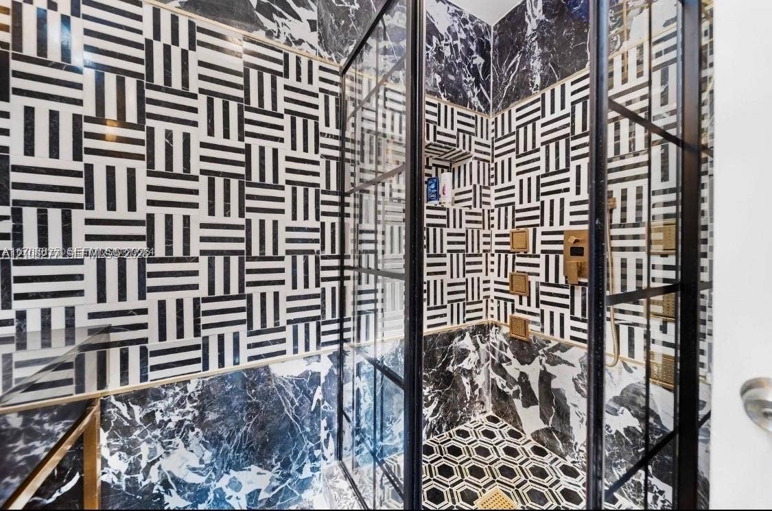 Walk-in shower featuring geometric black-and-white tile walls, contrasting veined stone lower walls, a built-in recessed niche, gold-tone hardware, and a black-framed glass enclosure
