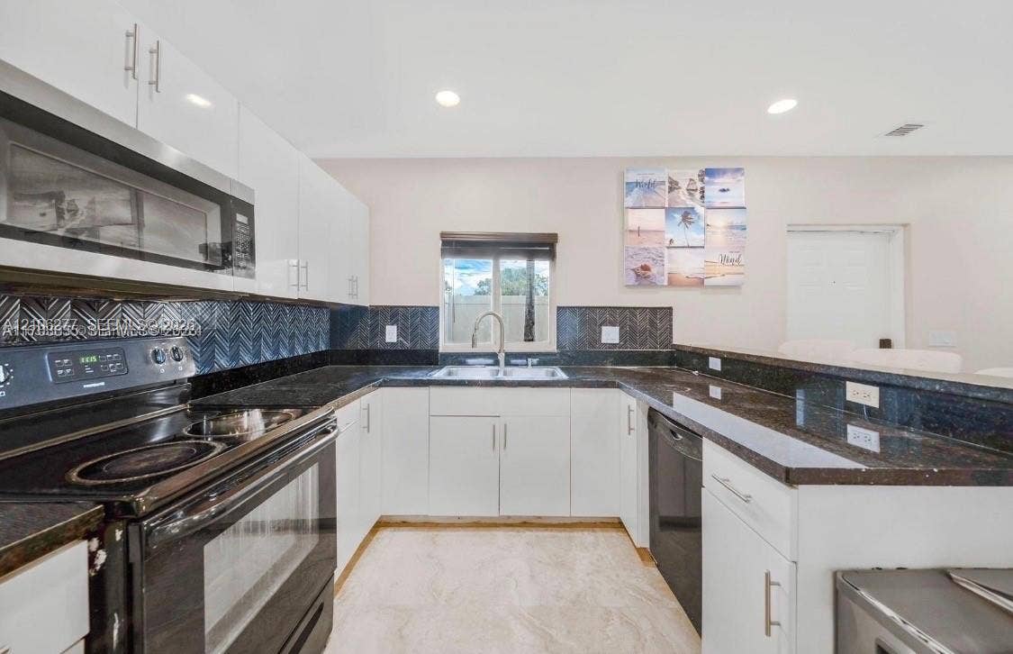 Kitchen featuring high-gloss white cabinetry, dark stone-finish countertops, herringbone-patterned tile backsplash, stainless steel appliances, and tile flooring