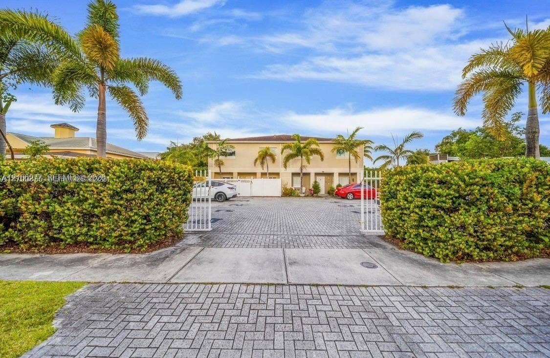 Exterior facade featuring stucco finish and paver-stone driveway with secured gated entrance