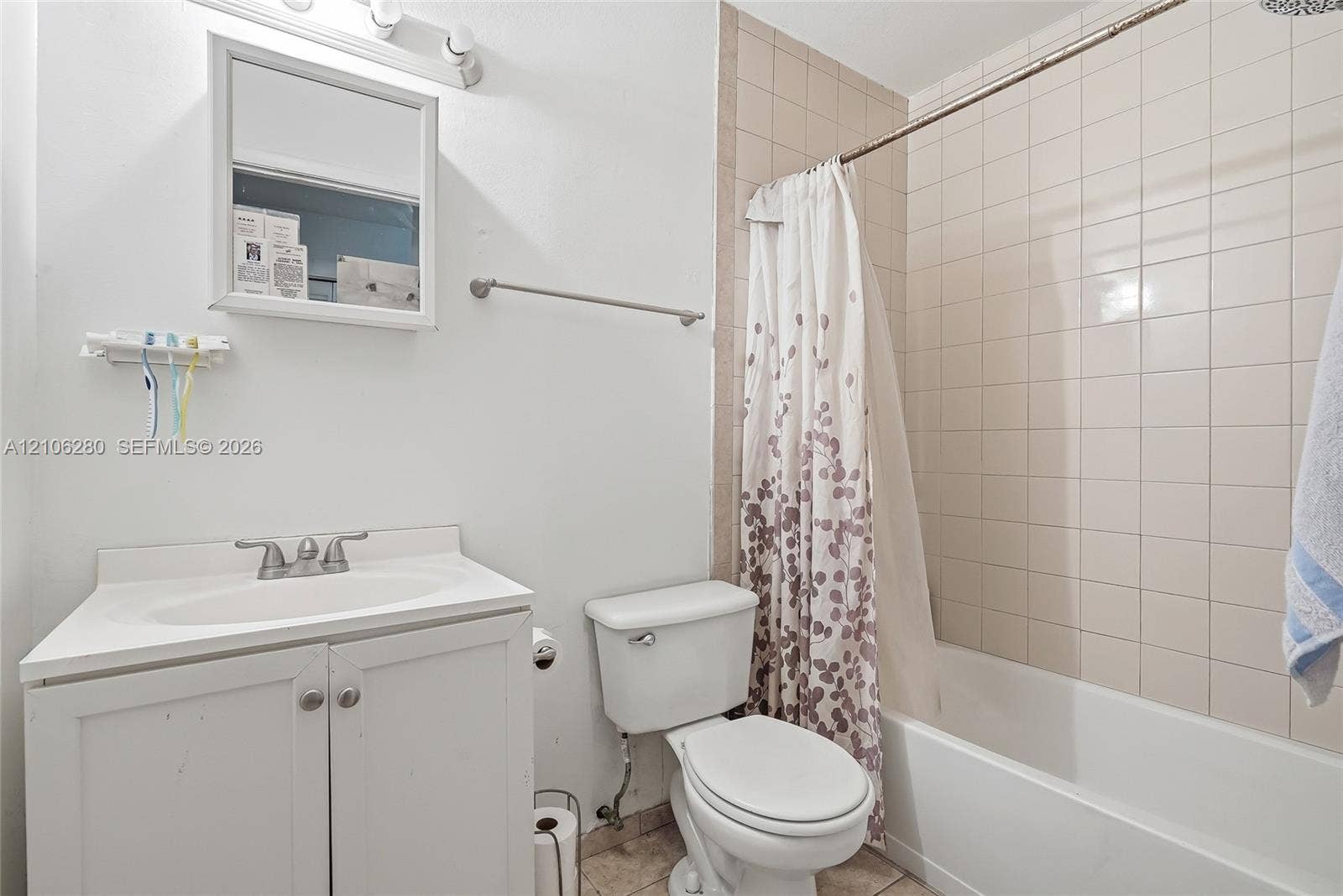 2017 SE Ancora Court, Port St Lucie, FL 34952 Bathroom featuring a white vanity cabinet with a drop-in sink, a wall-mounted medicine cabinet, a tiled shower surround, and a porcelain tub