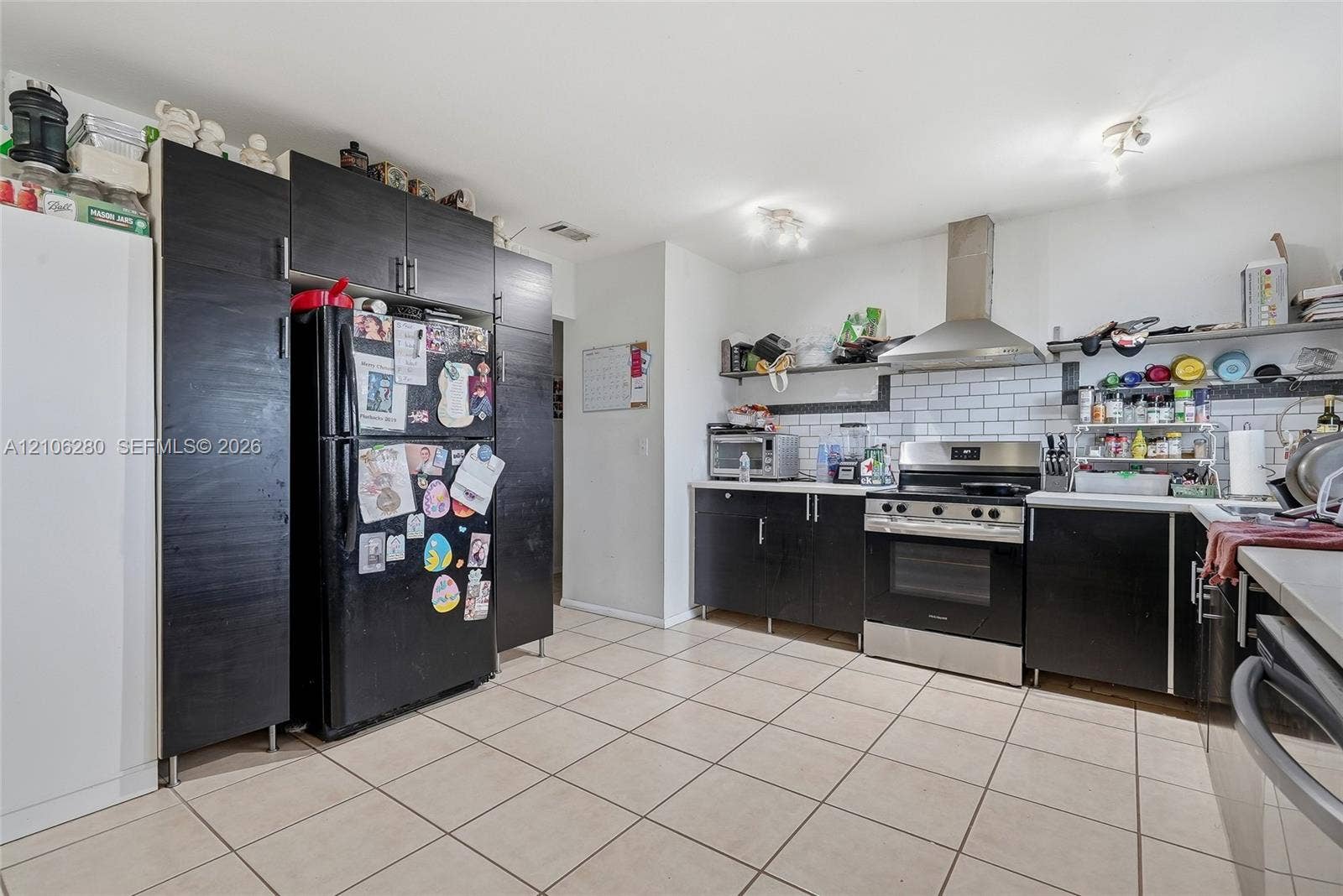 2017 SE Ancora Court, Port St Lucie, FL 34952 Kitchen featuring dark-finish cabinetry, stainless steel range with overhead vent hood, white subway tile backsplash, and light-tone tile flooring