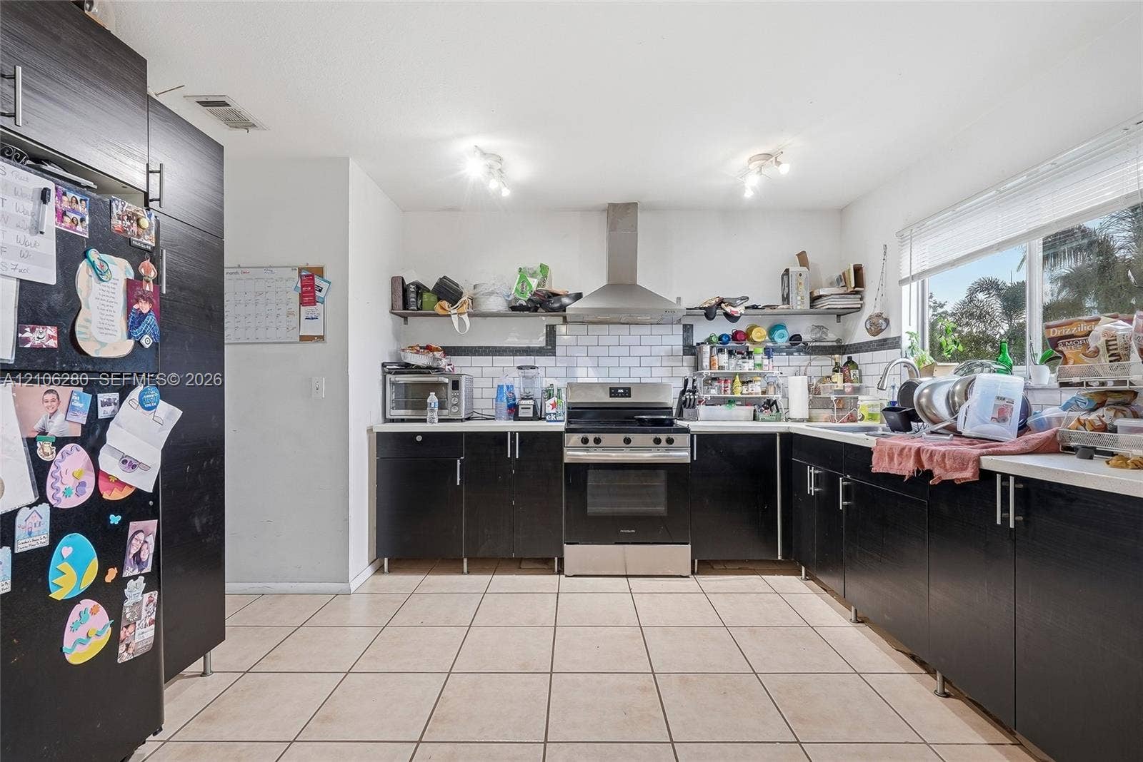 2017 SE Ancora Court, Port St Lucie, FL 34952 Kitchen featuring dark cabinetry, stainless steel range with overhead vent hood, white subway tile backsplash, and ceramic tile flooring
