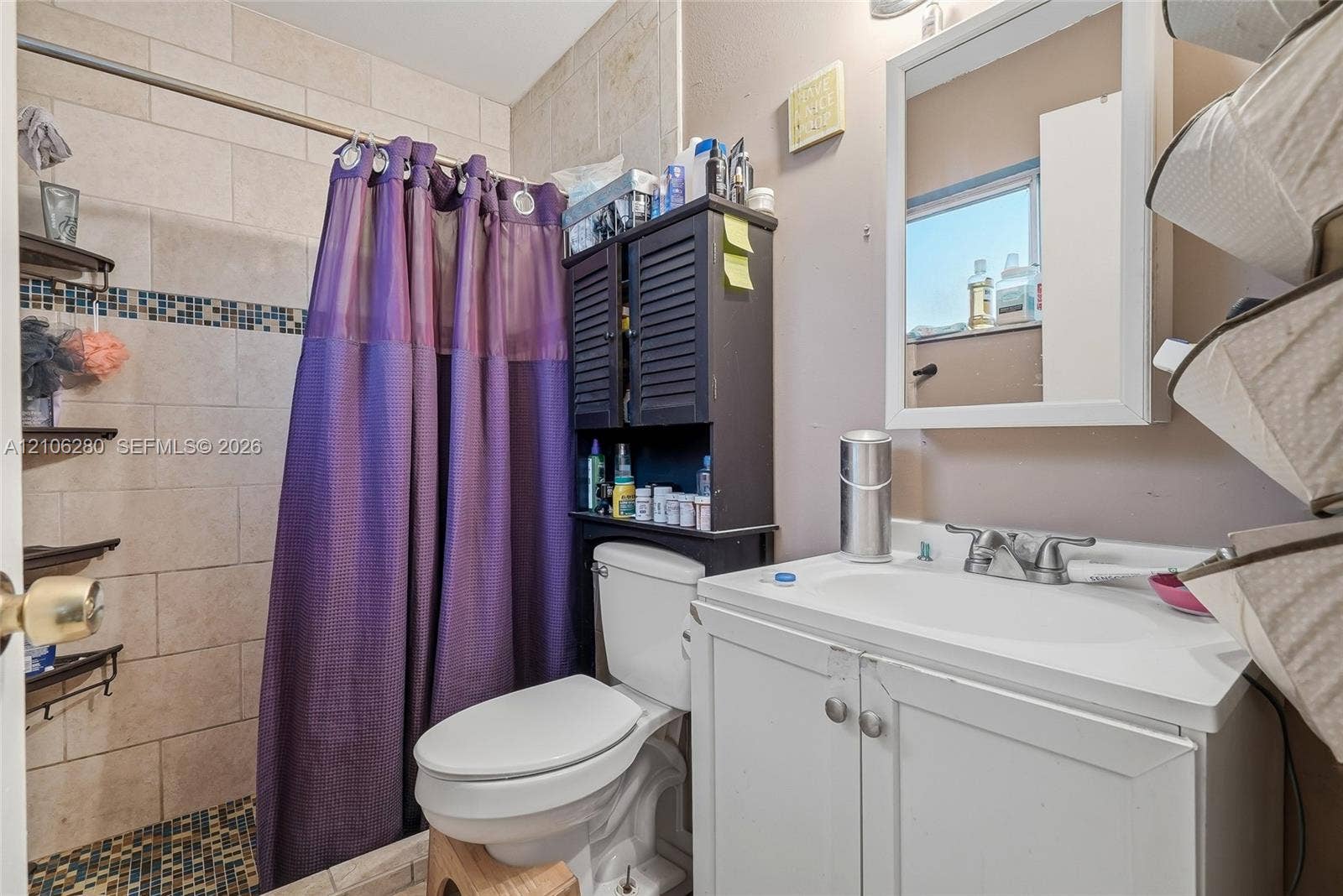 2017 SE Ancora Court, Port St Lucie, FL 34952 Bathroom featuring a white vanity cabinet with an integrated sink, wall-mounted mirrored medicine cabinet, and shower area with tiled walls and decorative glass tile inlay