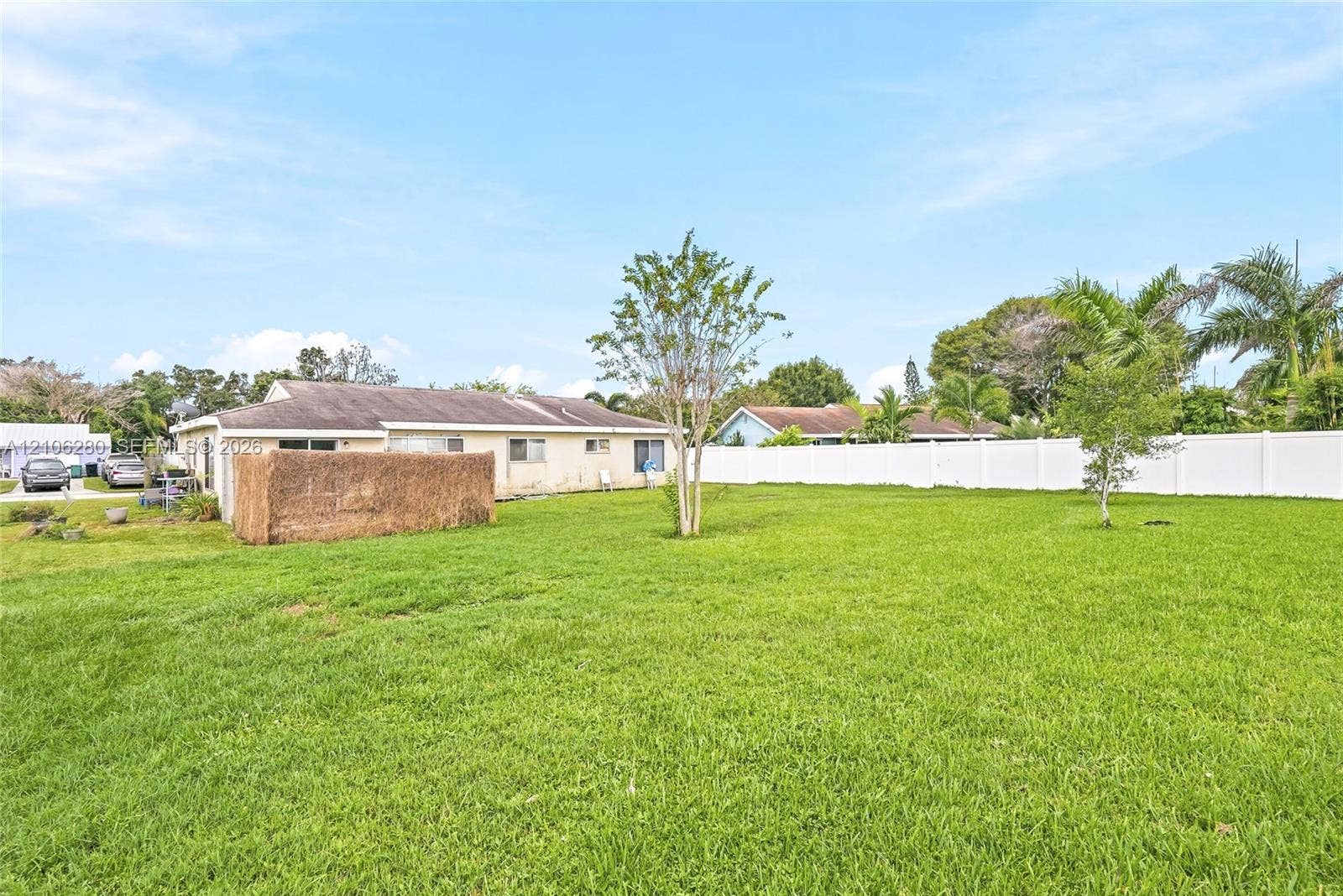 2017 SE Ancora Court, Port St Lucie, FL 34952 Expansive backyard featuring a large grass lawn, mature trees, and a full-perimeter white vinyl privacy fence
