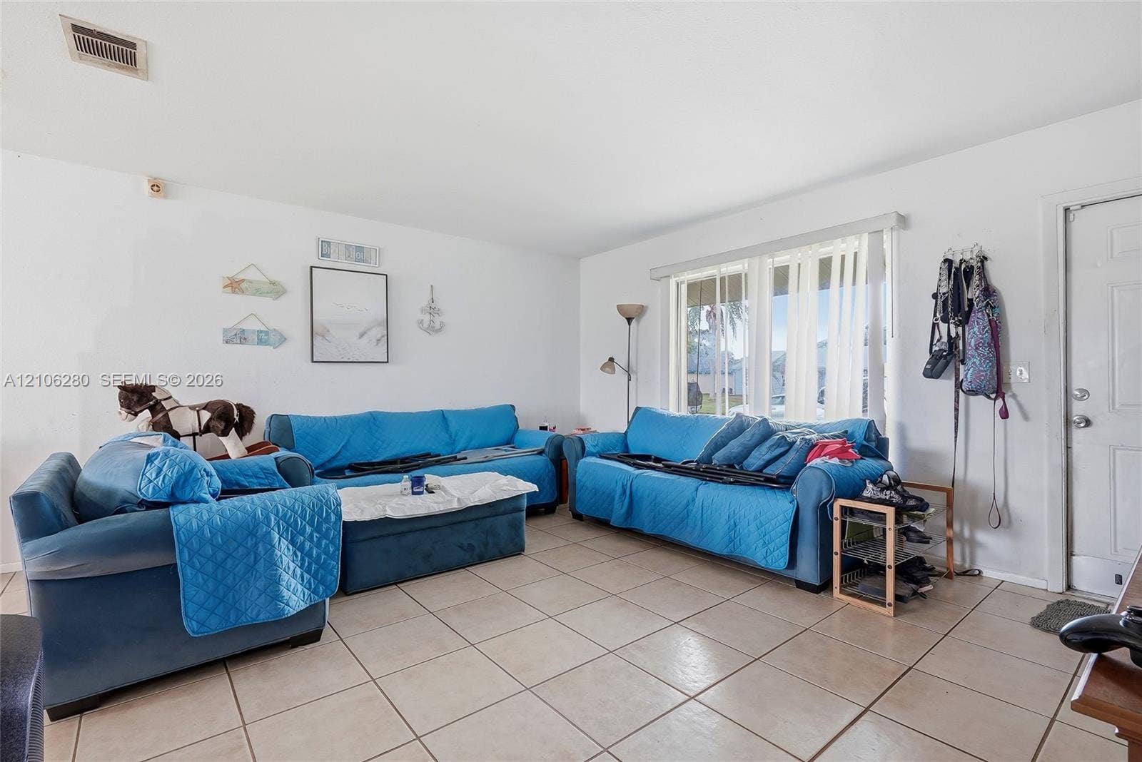 2017 SE Ancora Court, Port St Lucie, FL 34952 Living area featuring large-format tile flooring, neutral wall tones, and a multi-pane window with vertical blinds