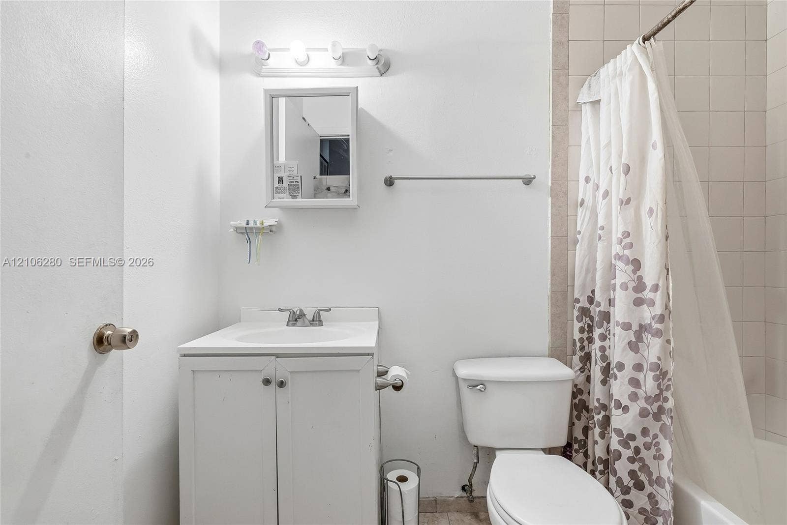 2017 SE Ancora Court, Port St Lucie, FL 34952 Bathroom featuring a white vanity with integrated basin, wall-mounted medicine cabinet, multi-bulb vanity light, and a tiled tub surround