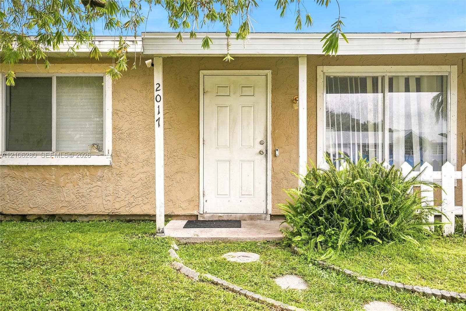 2017 SE Ancora Court, Port St Lucie, FL 34952 Stucco exterior featuring a covered front entryway, white picket fencing, and a stone-paver walkway