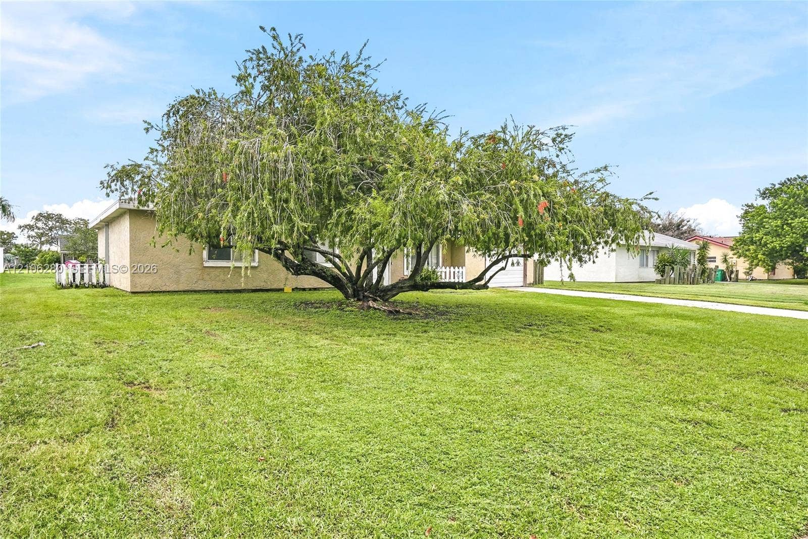 2017 SE Ancora Court, Port St Lucie, FL 34952 Stucco exterior featuring an expansive front lawn, mature specimen tree, and white picket fencing