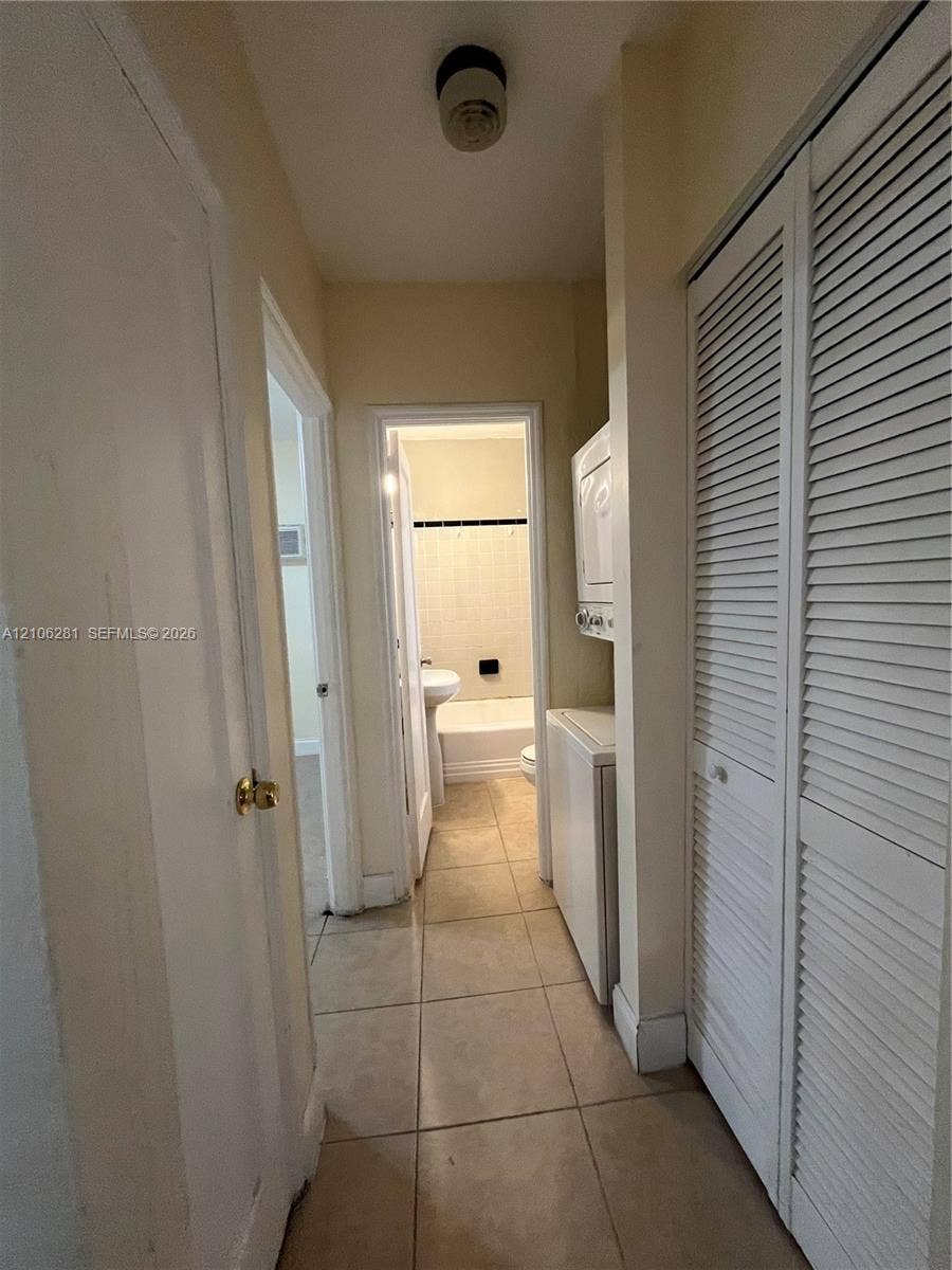 832 SW 31st Avenue, #832, Miami, Miami, FL 33135 Utility area featuring large-format tile flooring, louvered bi-fold closet doors, and a stackable appliance unit
