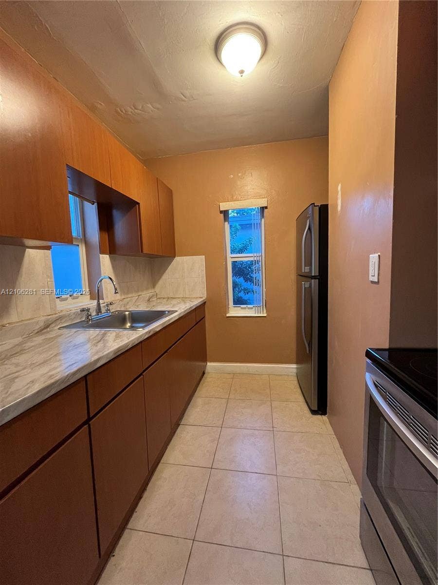 832 SW 31st Avenue, #832, Miami, Miami, FL 33135 Galley kitchen featuring wood-finish cabinetry, stone-pattern laminate countertops, stainless steel sink with a gooseneck faucet, tile flooring, and stainless steel appliances