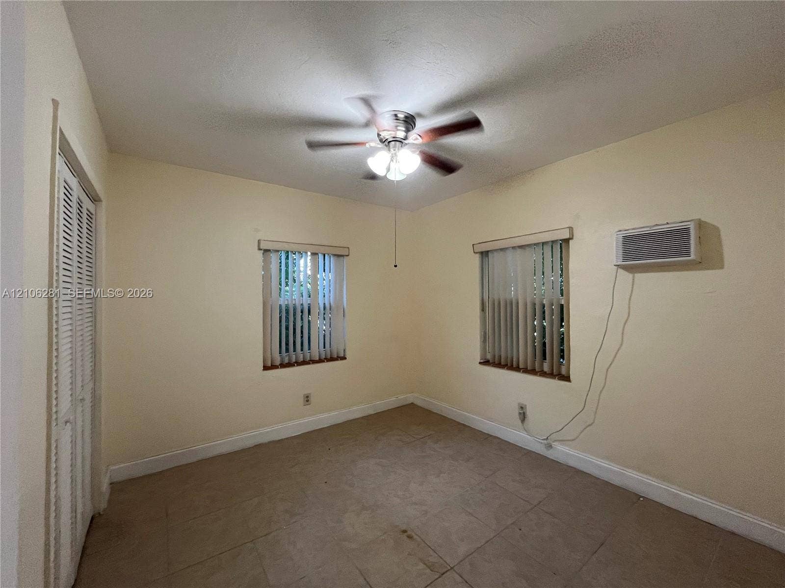 832 SW 31st Avenue, #832, Miami, Miami, FL 33135 Interior space featuring ceramic tile flooring, a multi-blade ceiling fan with integrated lighting, two windows with vertical blinds, and a wall-mounted climate control unit