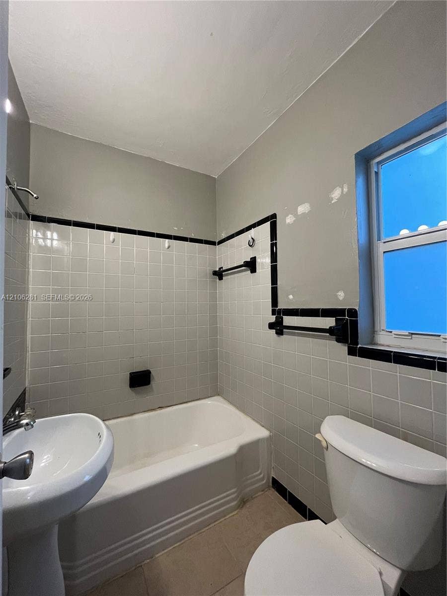 832 SW 31st Avenue, #832, Miami, Miami, FL 33135 Bathroom featuring a white pedestal sink, a deep-basin soaking tub, square-tiled wall surround with decorative black trim, and wall-mounted towel hardware